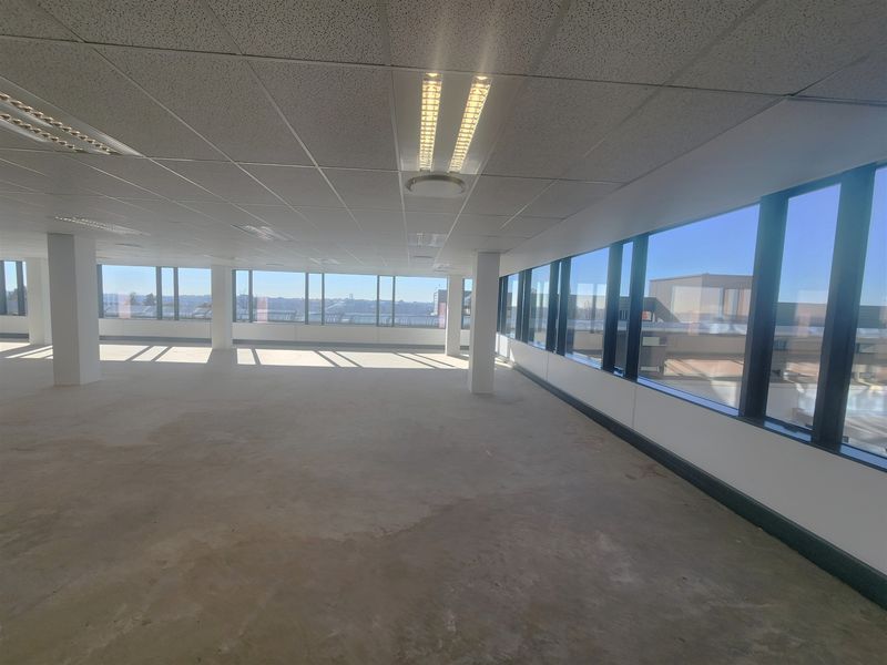 A spacious, open-plan office area featuring large windows with natural light, suspended ceilings, and unfinished concrete flooring, ready for custom fit-out.