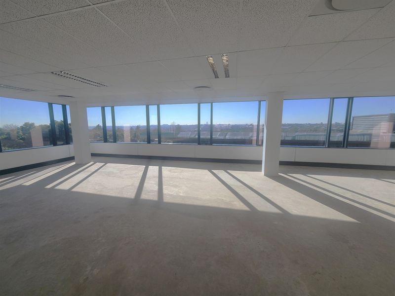 A bright, open-plan office space featuring large floor-to-ceiling windows, suspended ceilings, and recessed lighting, offering an expansive view.