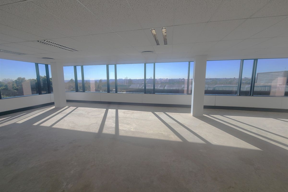 A bright, open-plan office space featuring large floor-to-ceiling windows, suspended ceilings, and recessed lighting, offering an expansive view.