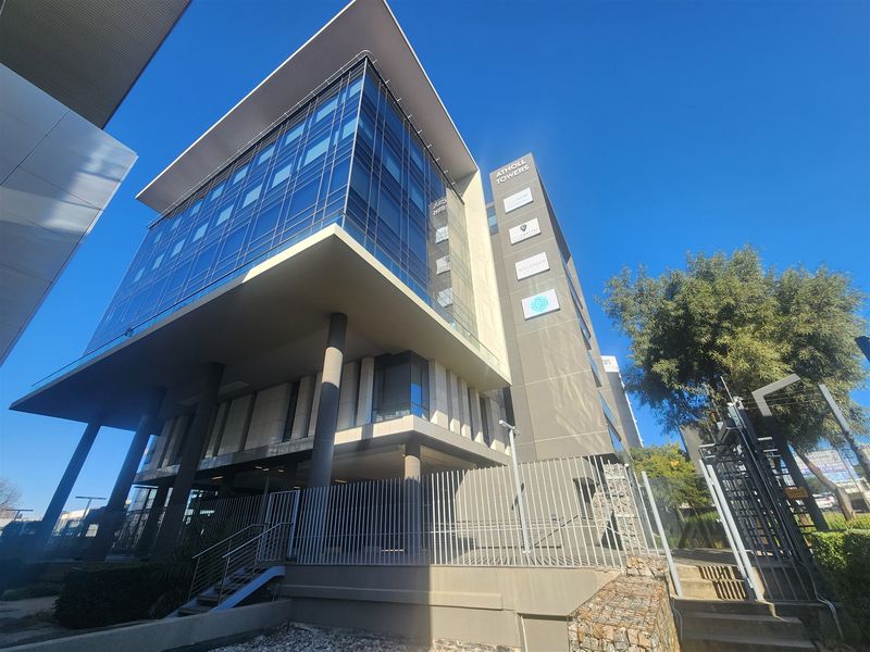 Modern multi-story office building featuring a glass facade, concrete structural elements, and secure perimeter fencing.