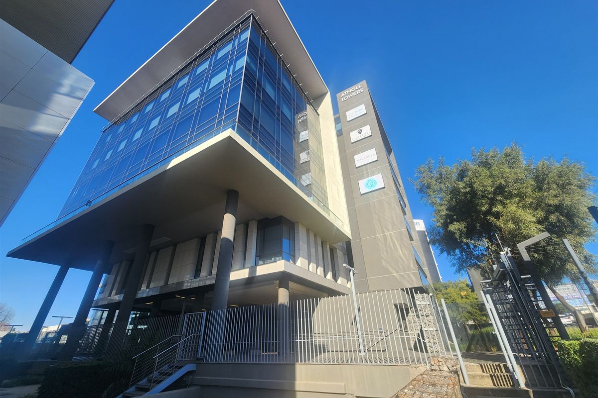 Modern multi-story office building featuring a glass facade, concrete structural elements, and secure perimeter fencing.