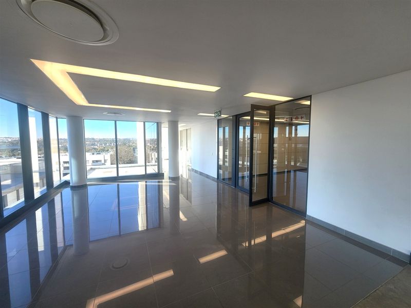 Modern, open-plan office space featuring polished floor tiles, recessed ceiling lighting, and floor-to-ceiling glass partitions with expansive views.