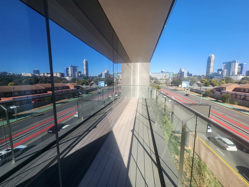 Modern balcony featuring a sleek glass balustrade and composite decking, offering expansive views of the surrounding cityscape and major road infrastructure.