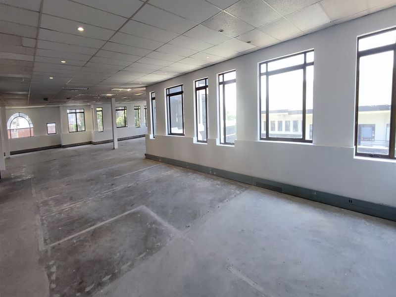 Spacious open-plan office area featuring a suspended ceiling, recessed lighting, and large windows providing ample natural light, currently in a shell condition.