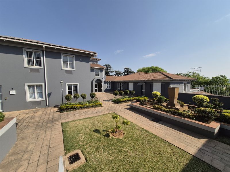 A well-maintained office complex courtyard featuring paved walkways, landscaped garden beds, and a central water feature area.