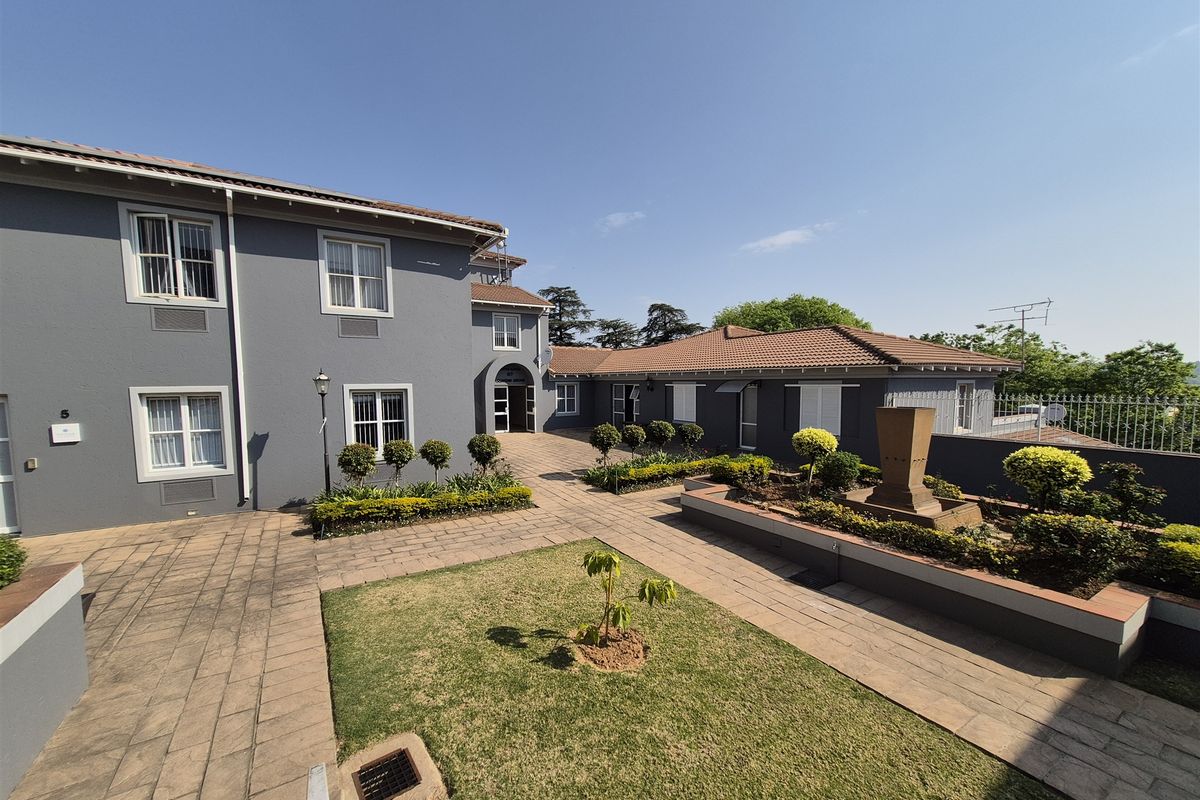 A well-maintained office complex courtyard featuring paved walkways, landscaped garden beds, and a central water feature area.