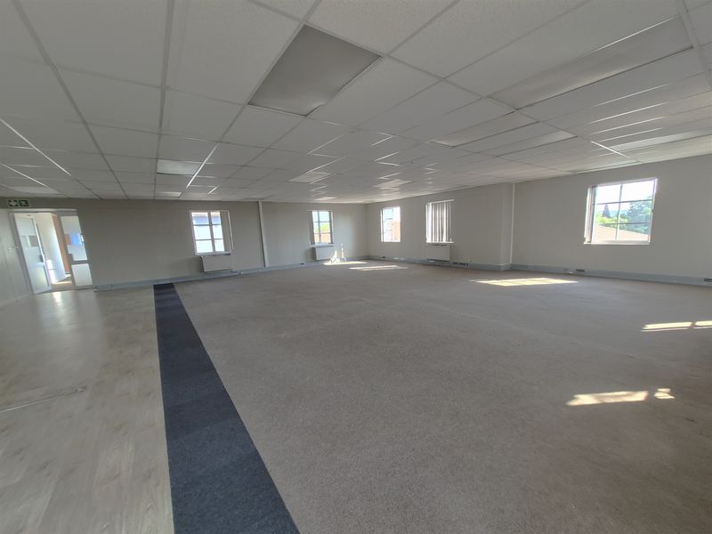 Spacious, open-plan office area featuring a suspended ceiling, mixed carpet and laminate flooring, and multiple windows providing natural light.