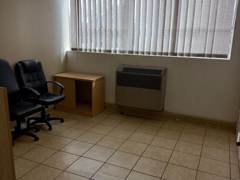 A functional office space featuring ceramic tile flooring, a built-in HVAC unit, and vertical window blinds, providing a practical work environment.