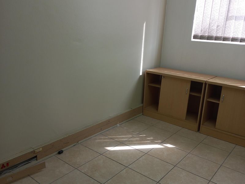 A vacant office space featuring tiled flooring, built-in cabinetry, and vertical window blinds, requiring minor repairs to baseboards and electrical finishes.