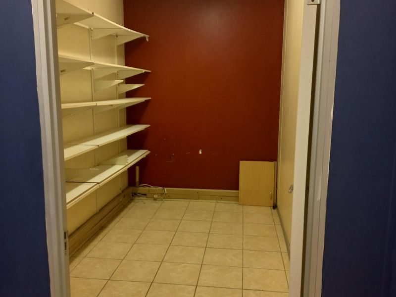 A small utility or storage room featuring tiled flooring, built-in shelving units, and overhead fluorescent lighting.
