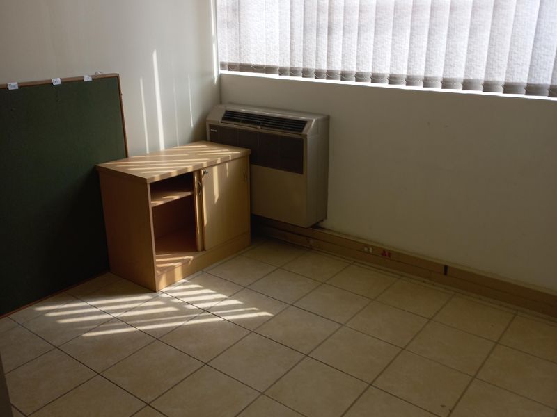 A functional office space featuring tiled flooring, vertical window blinds, and a wall-mounted air conditioning unit.