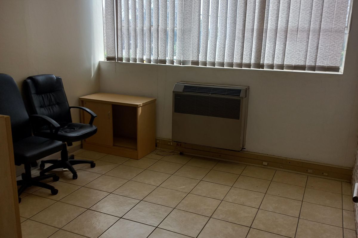 A functional office space featuring ceramic tile flooring, a built-in HVAC unit, and vertical window blinds, providing a practical work environment.