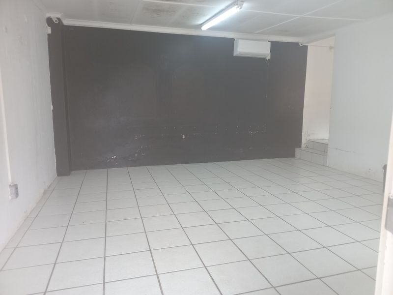 An empty office space featuring ceramic floor tiles, a split-system air conditioner, and a dark feature wall with visible wear and tear.