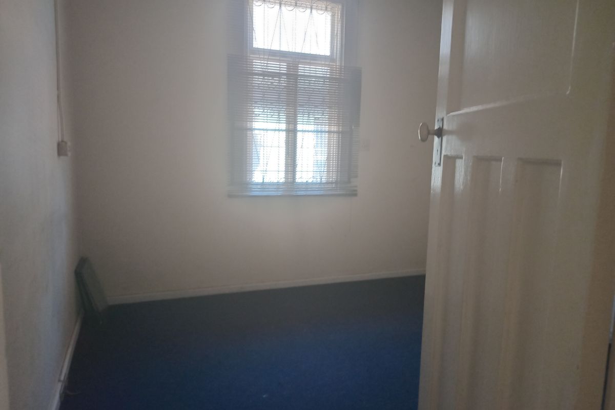 An empty office space featuring carpeted flooring, a window with blinds, and a white panel door.