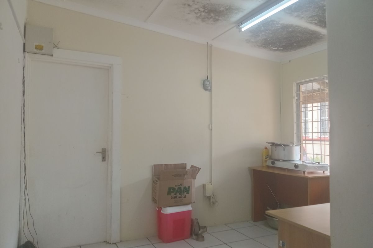 A small kitchen area featuring tiled flooring and security bars on the window, currently showing significant ceiling staining and requiring maintenance.
