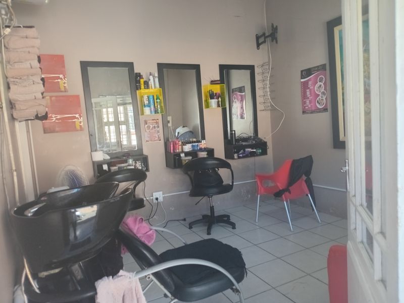 A functional commercial space currently utilized as a salon, featuring tiled flooring, wall-mounted mirrors, and dedicated utility areas for professional services.