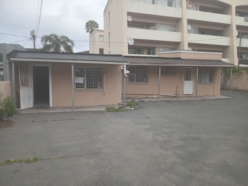 Exterior view of a single-story office building featuring a corrugated metal roof, security bars on windows, and an asphalt parking area.