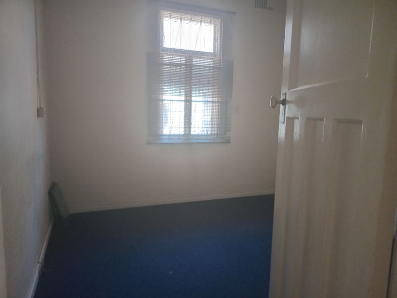 An empty office space featuring carpeted flooring, a window with blinds, and a white panel door.