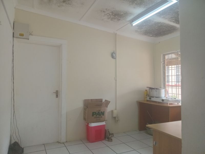 A small kitchen area featuring tiled flooring and security bars on the window, currently showing significant ceiling staining and requiring maintenance.
