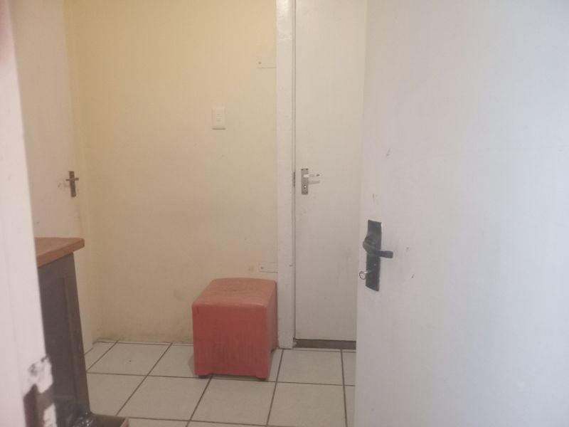 A small, functional hallway area featuring tiled flooring and access to internal doors, currently presenting in a dated condition.