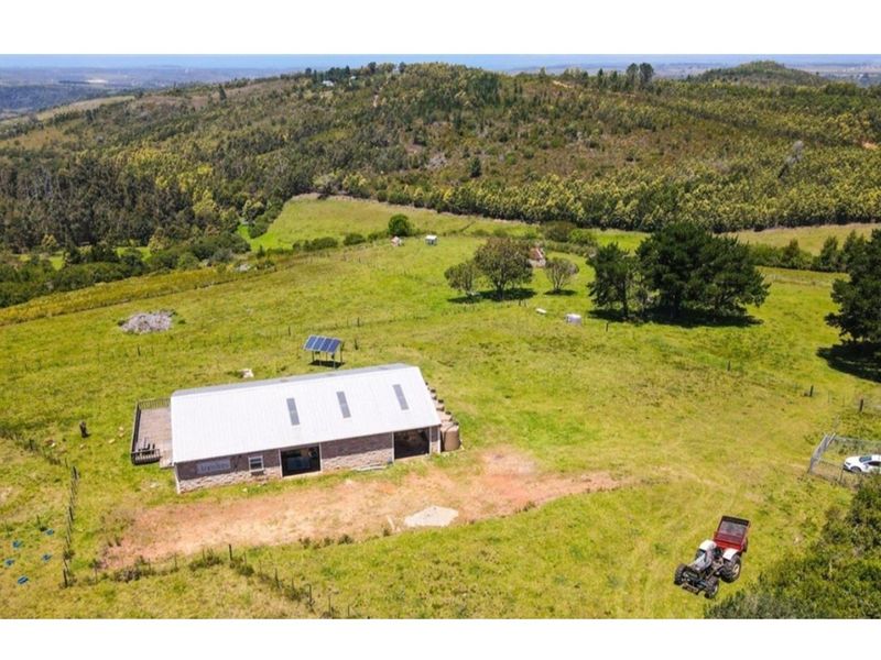 Aerial view of a rural farm property featuring a building with a metal roof, solar panels, and surrounding pasture land.
