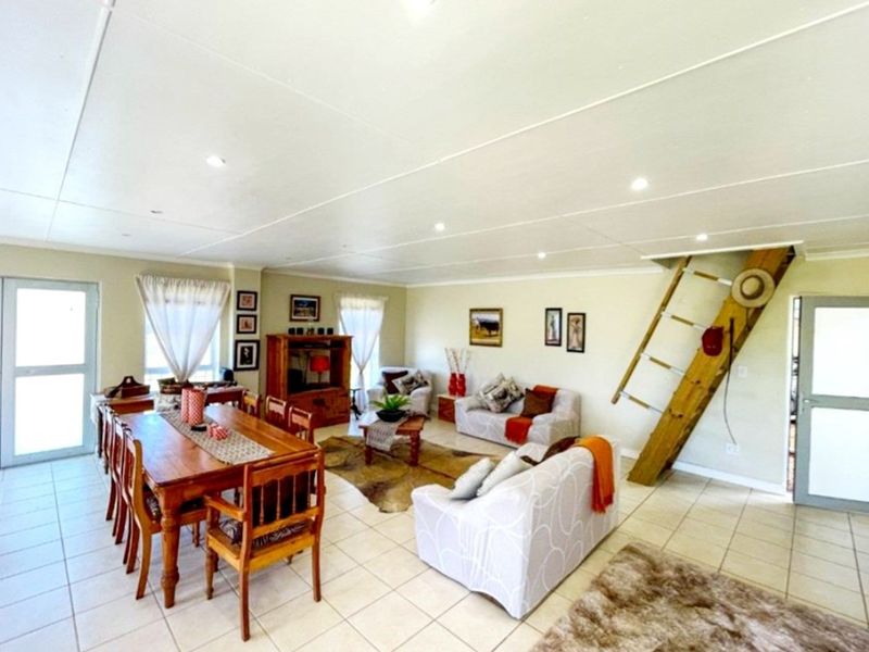 Spacious open-plan living and dining area featuring tiled flooring, recessed lighting, and a wooden staircase leading to an upper level.