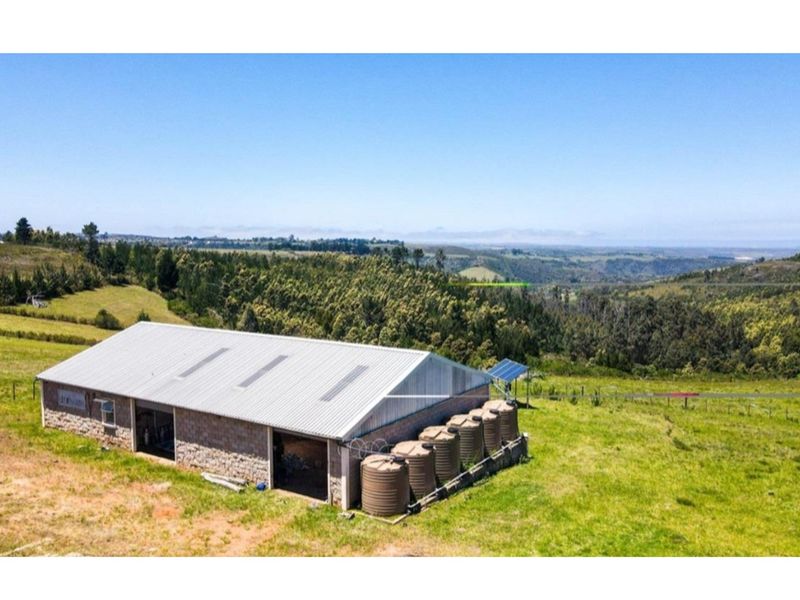 Aerial view of a farm outbuilding featuring stone masonry walls, a corrugated metal roof, solar panels, and multiple water storage tanks set in landscape.