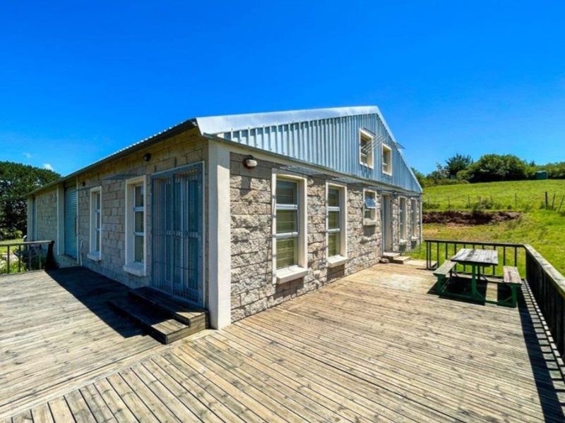 Rear view of a stone-clad farm building featuring an expansive timber deck and corrugated metal roof, set against a rural landscape.