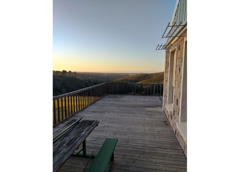 Spacious timber deck featuring a balustrade and stone-clad exterior wall, offering expansive views of the surrounding rural landscape.