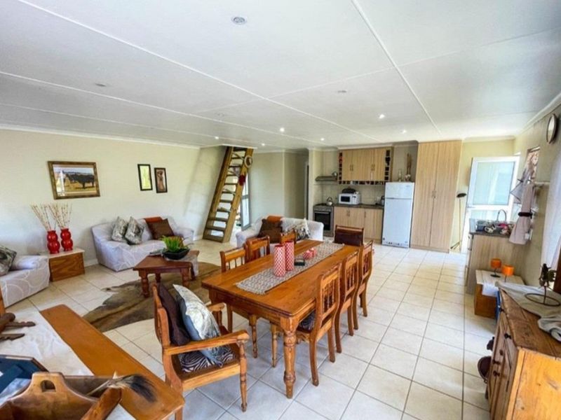 Spacious open-plan living and dining area featuring tiled floors, a functional kitchen with built-in cabinetry, and a staircase leading to an upper level.