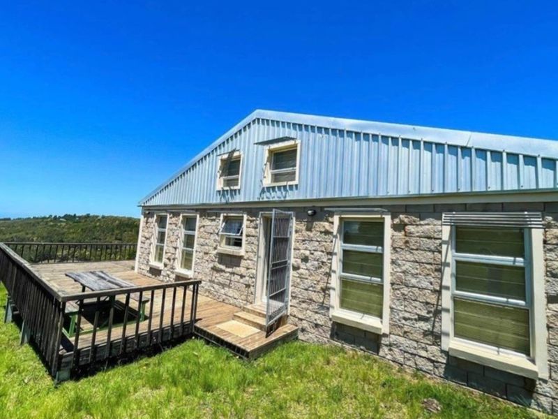 Rear view of a stone-clad farmhouse featuring a timber deck, corrugated metal roof, and expansive rural landscape views.