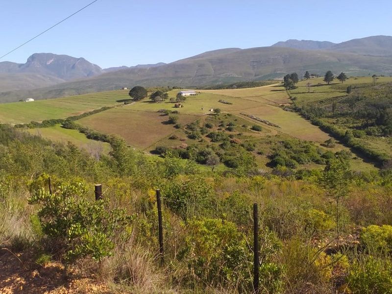 A scenic elevated view of the expansive farm landscape featuring rolling hills, natural vegetation, and distant mountain ranges.