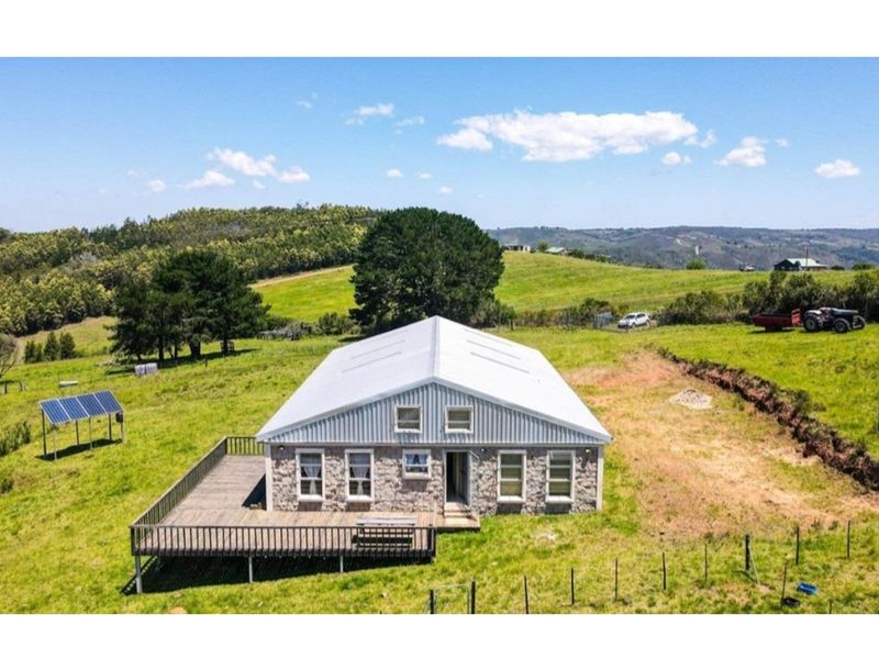 Aerial view of a stone-clad farmhouse featuring a metal roof, expansive timber deck, and solar panel installation set within a rural landscape.