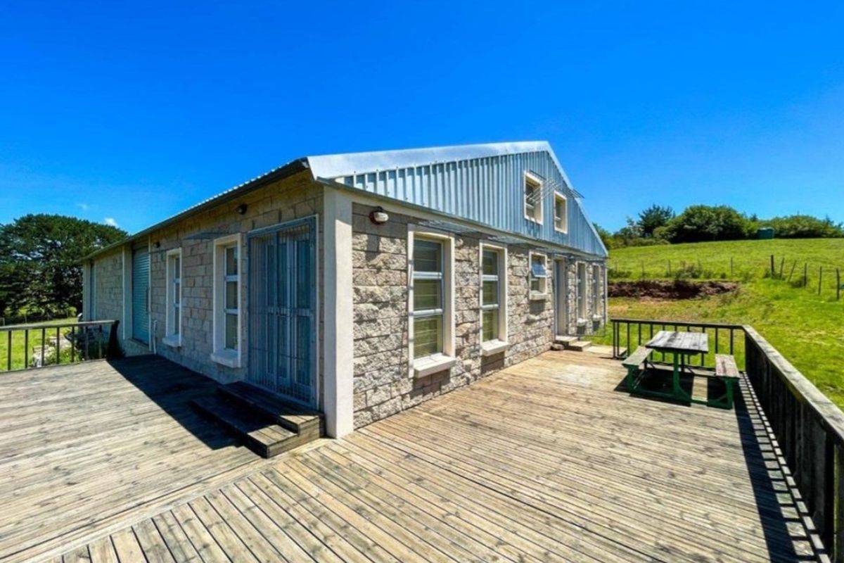 Rear view of a stone-clad farm building featuring an expansive timber deck and corrugated metal roof, set against a rural landscape.