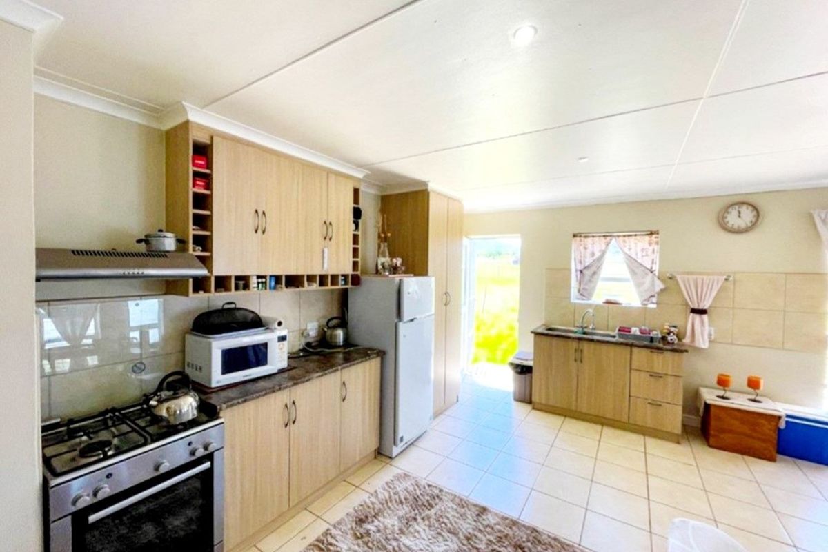 A functional kitchen featuring light wood-finish cabinetry, laminate countertops, a gas stove with extractor fan, and tiled flooring with direct outdoor access.