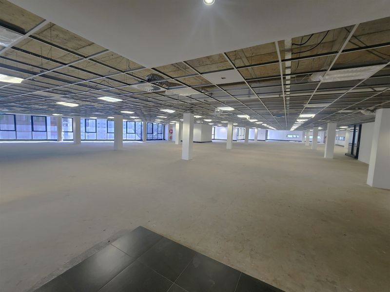 A large, open-plan office space featuring a suspended ceiling grid, structural columns, and expansive windows, currently in a shell condition ready for fit-out.