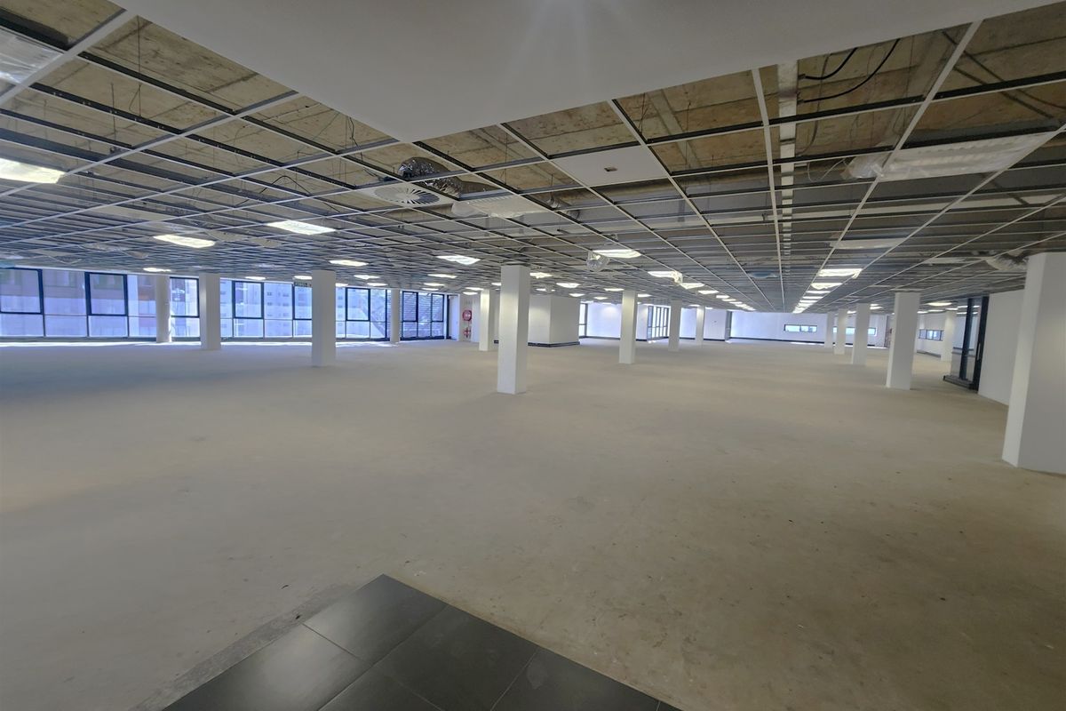 A large, open-plan office space featuring a suspended ceiling grid, structural columns, and expansive windows, currently in a shell condition ready for fit-out.