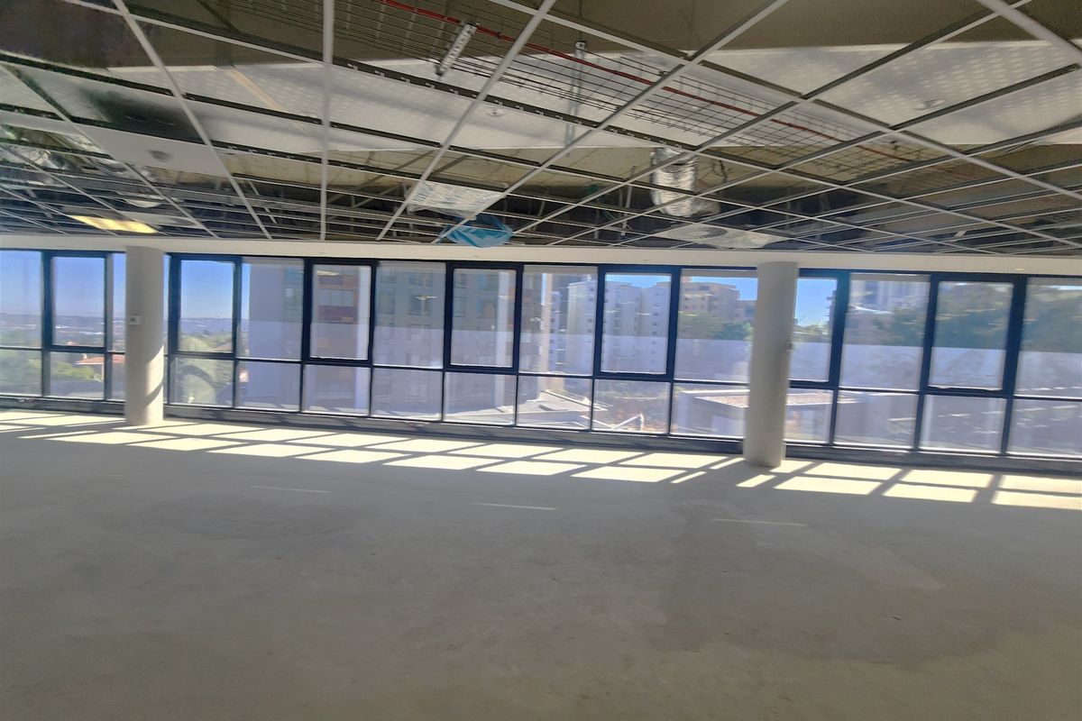 An open-plan office space in shell condition, featuring floor-to-ceiling windows, exposed ceiling grid, and unfinished flooring, ready for custom fit-out.