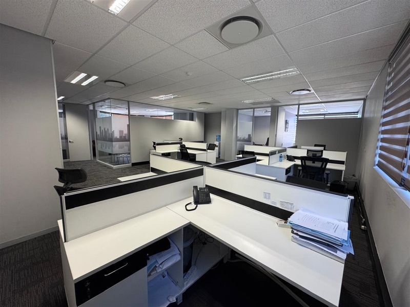 Modern open-plan office space featuring built-in desk workstations, glass partitions, suspended ceilings, and professional carpet flooring.