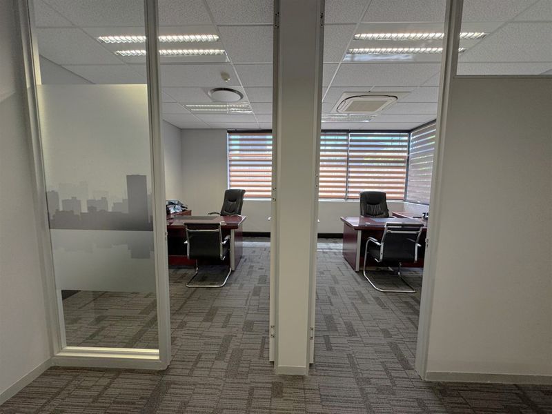 Professional office space featuring dual workstations, glass partition walls, carpeted flooring, and integrated ceiling lighting with ducted air conditioning.