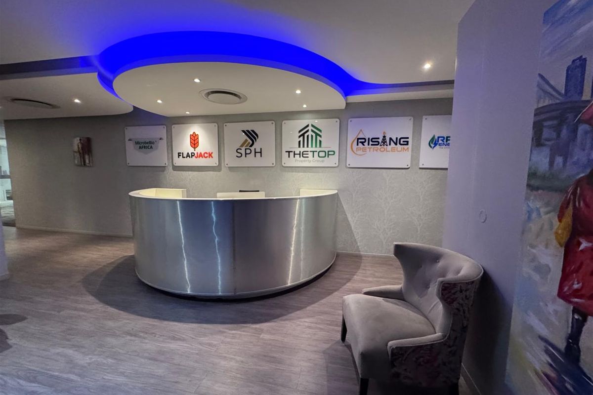 Modern office reception area featuring a curved metallic desk, recessed ceiling lighting with blue accent cove lighting, and wood-look laminate flooring.