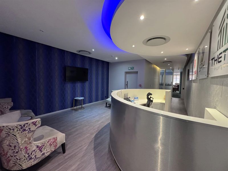 Modern office reception area featuring a curved metallic reception desk, decorative wallpaper, and integrated recessed ceiling lighting with blue accent cove lighting.