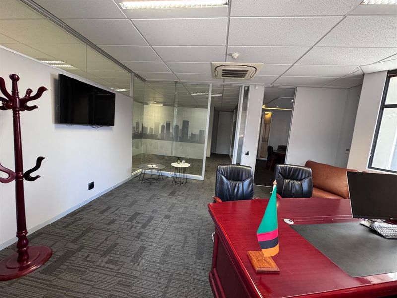 A professional office space featuring glass partitions, carpeted flooring, a suspended ceiling with integrated air conditioning, and a modern layout.