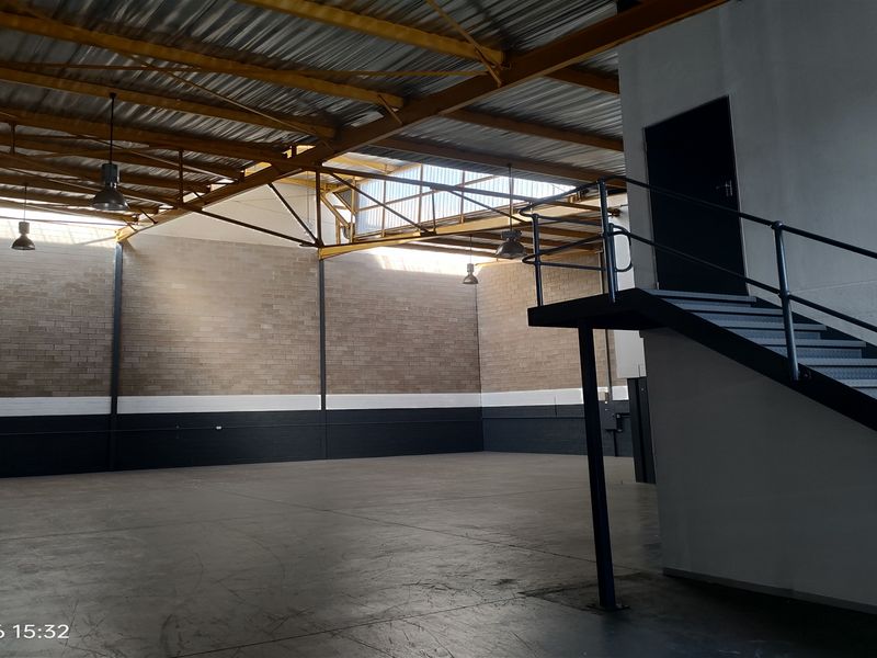 Spacious industrial warehouse unit featuring high ceilings with exposed steel trusses, concrete flooring, and a dedicated metal staircase leading to an upper level.