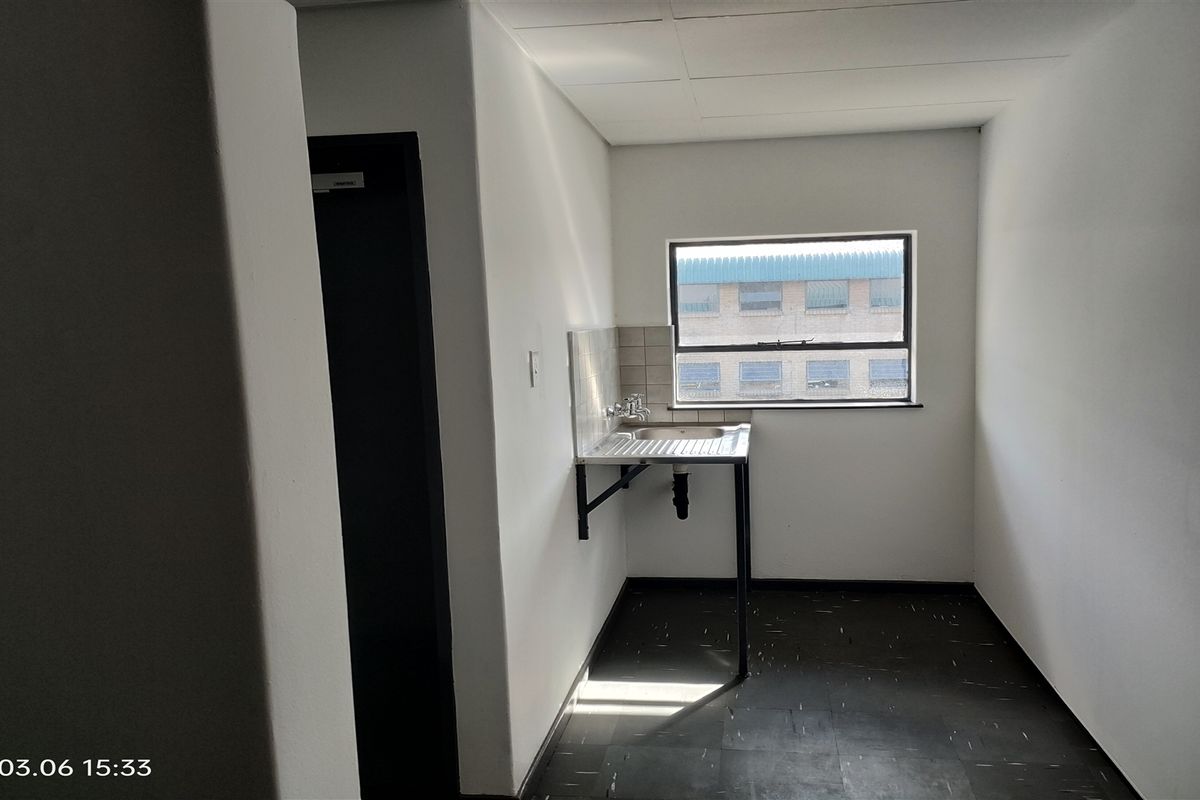 A compact, functional kitchenette area featuring a stainless steel sink, tiled splashback, and durable vinyl flooring in an industrial setting.
