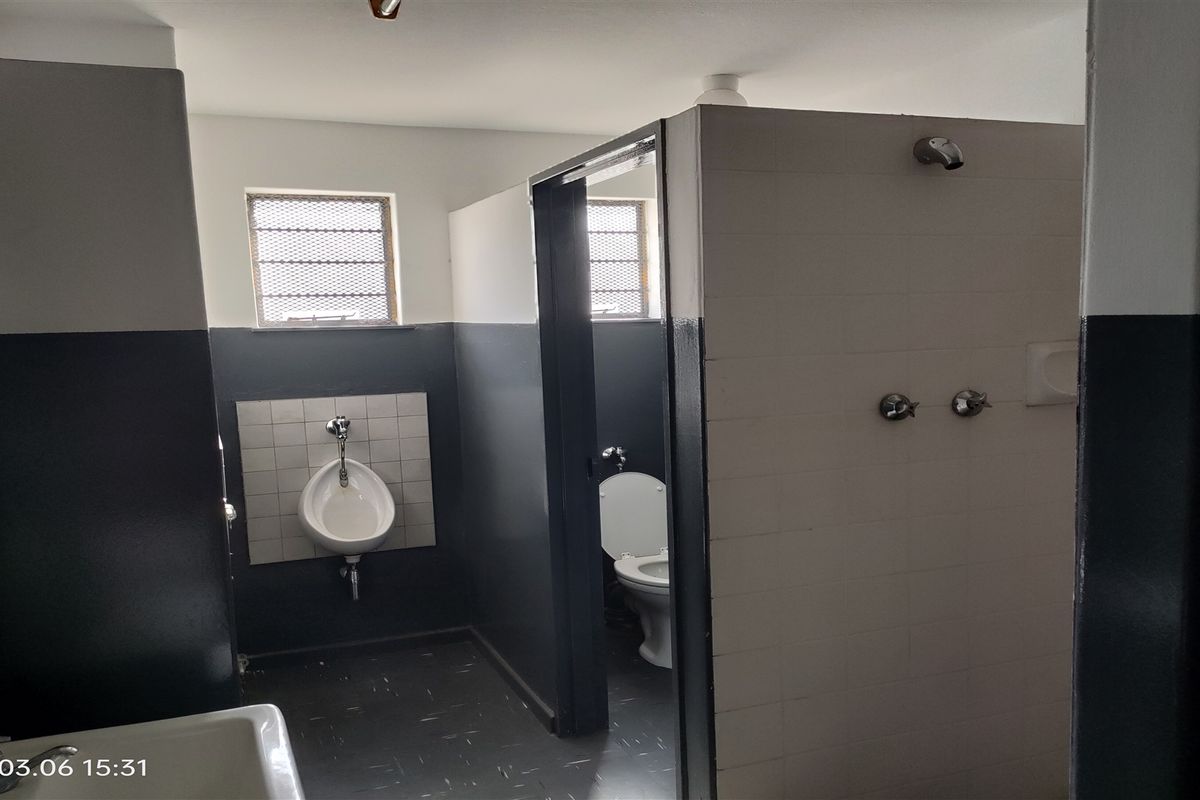 Industrial-style communal bathroom facility featuring a wall-mounted urinal, enclosed toilet cubicle, and shower plumbing fixtures.
