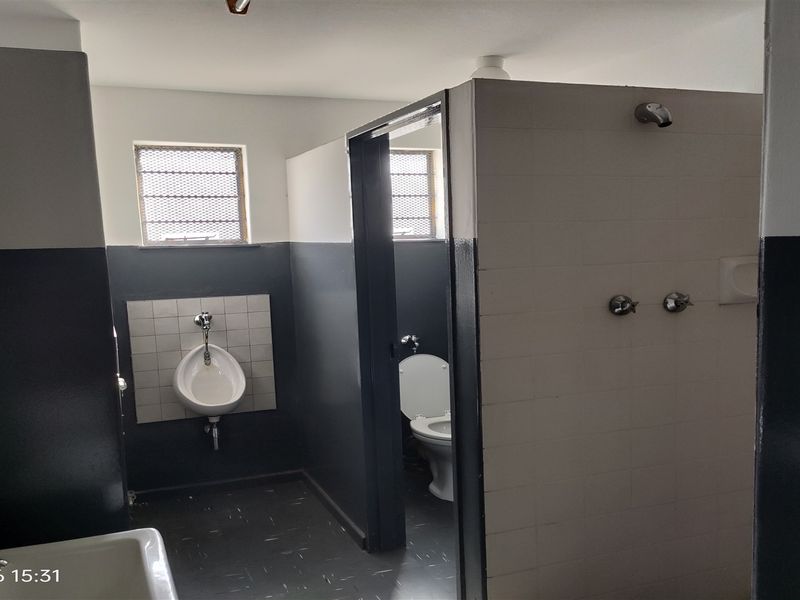 Industrial-style communal bathroom facility featuring a wall-mounted urinal, enclosed toilet cubicle, and shower plumbing fixtures.