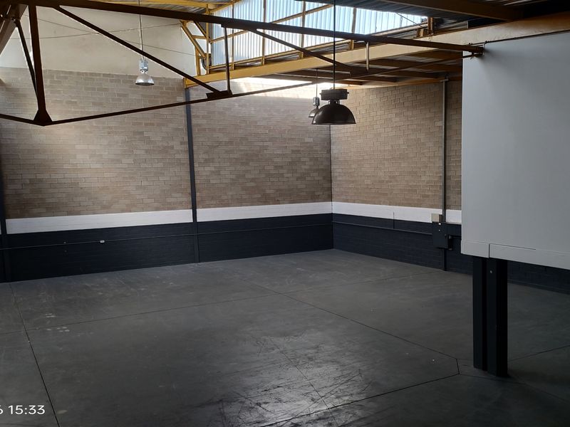 Spacious industrial utility area featuring exposed steel roof trusses, natural light from skylights, durable concrete flooring, and exposed brick walls.