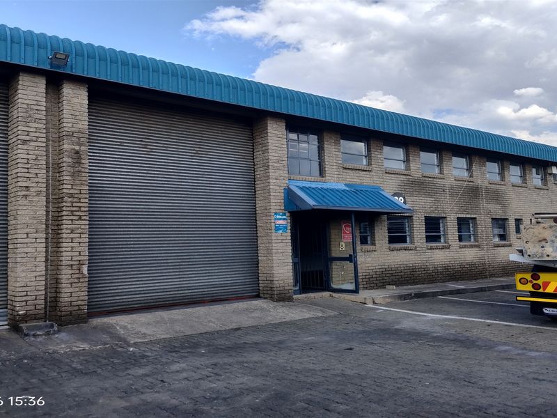 Industrial warehouse exterior featuring a large roller shutter door, brick facade, and metal roofing with an entrance awning.