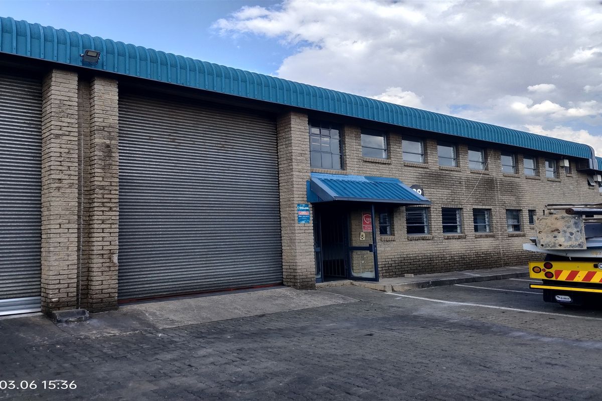 Industrial warehouse exterior featuring a large roller shutter door, brick facade, and metal roofing with an entrance awning.